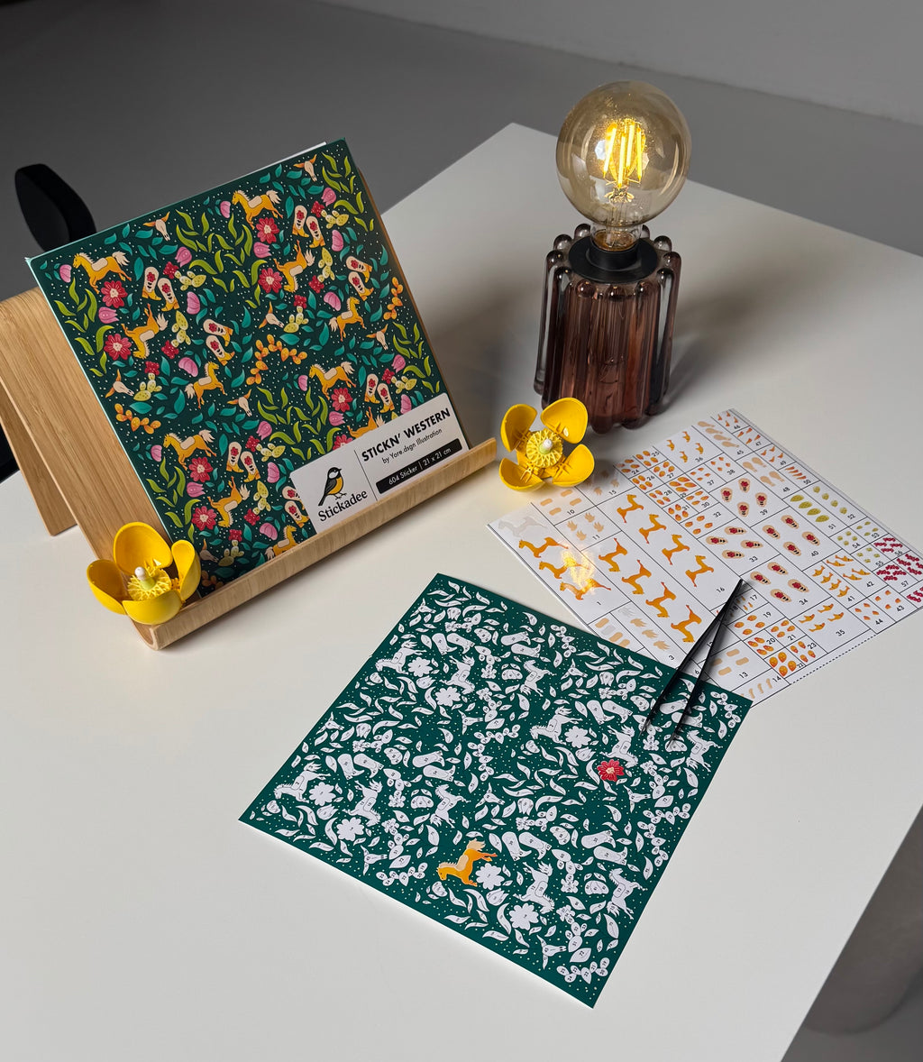 Sticker sheets with floral and animal patterns on a white surface with a lamp.